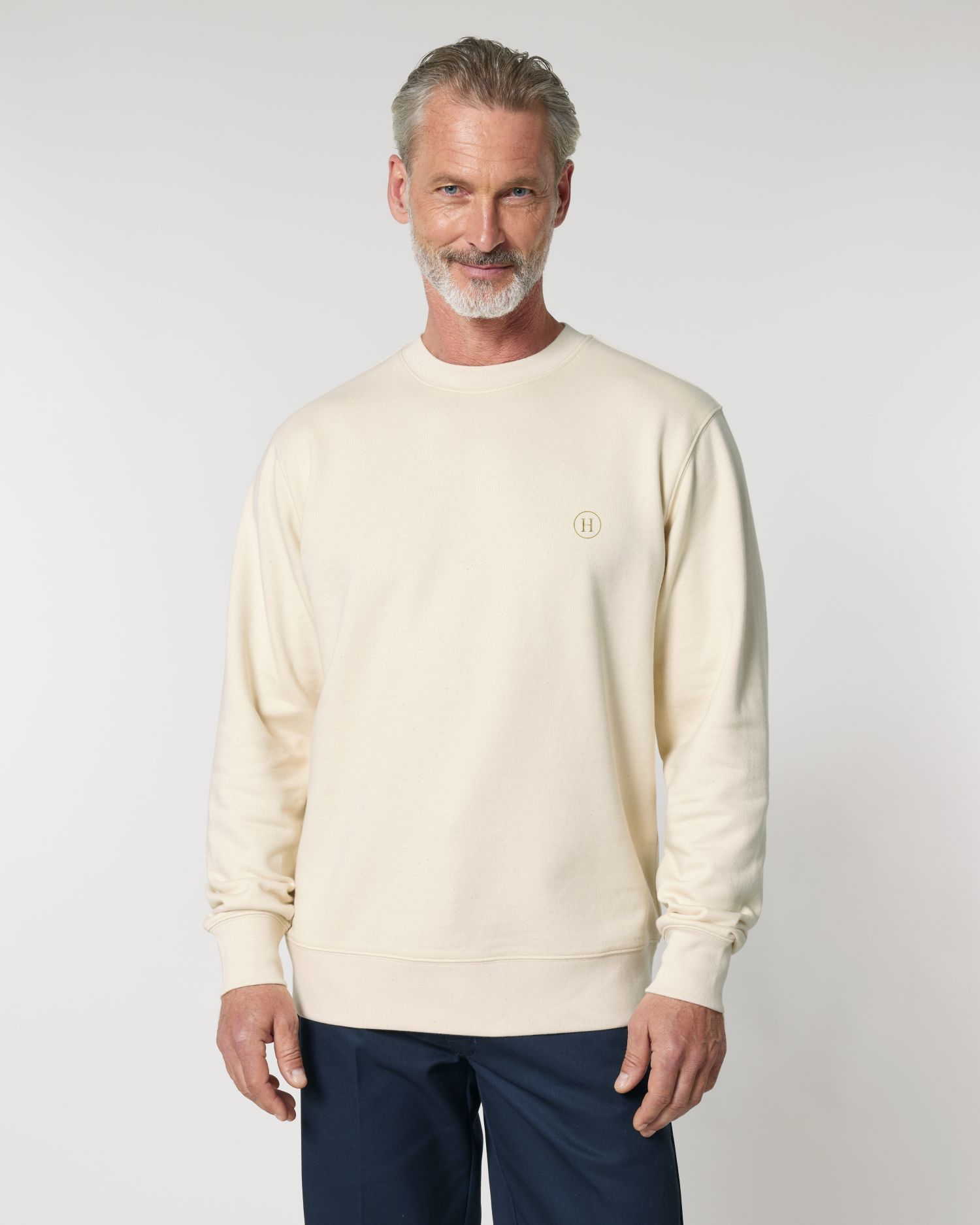 Man wearing a beige sweater and dark pants against a light gray background