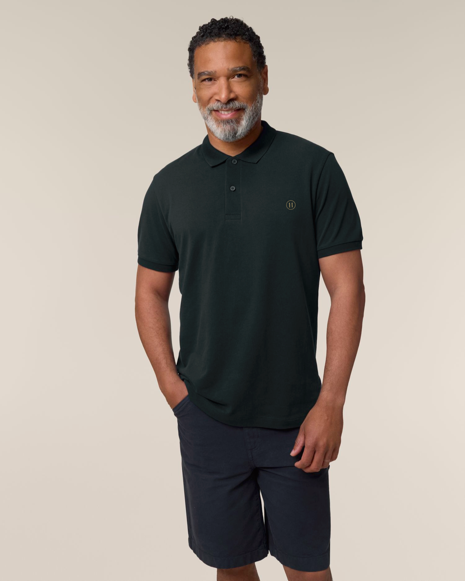 Man wearing a dark green polo shirt and navy shorts on a beige background