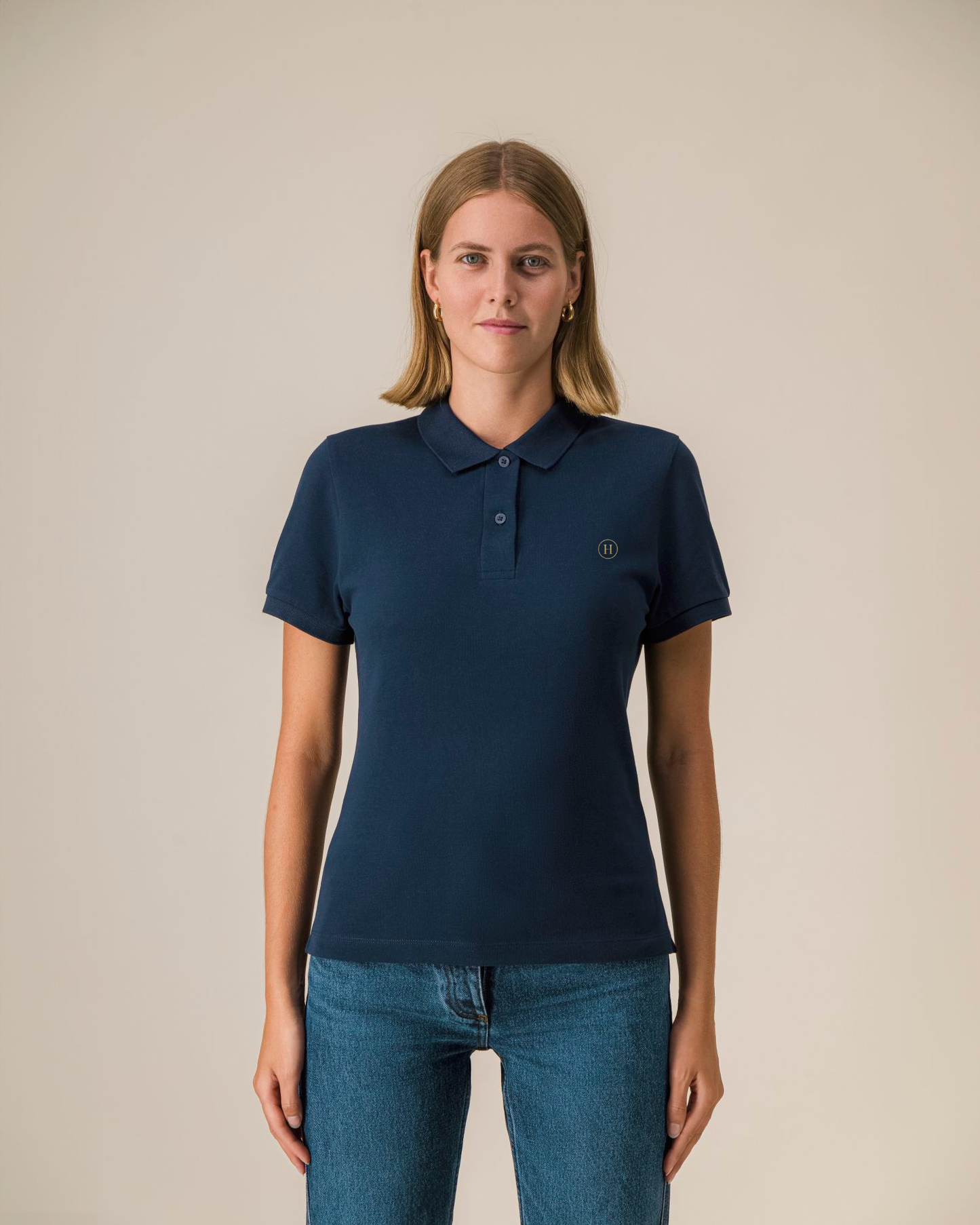 Woman wearing a navy blue polo shirt with a small logo on a beige background