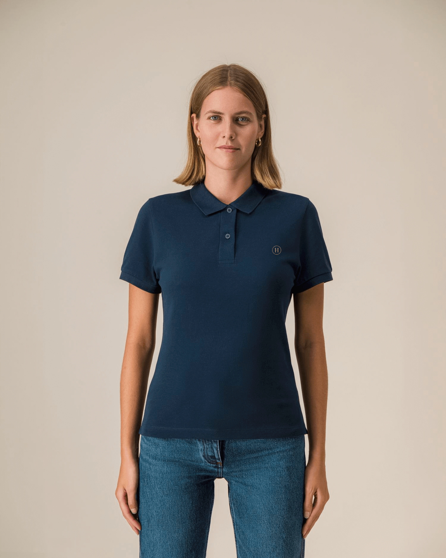Woman wearing a navy blue polo shirt with a small logo on a beige background