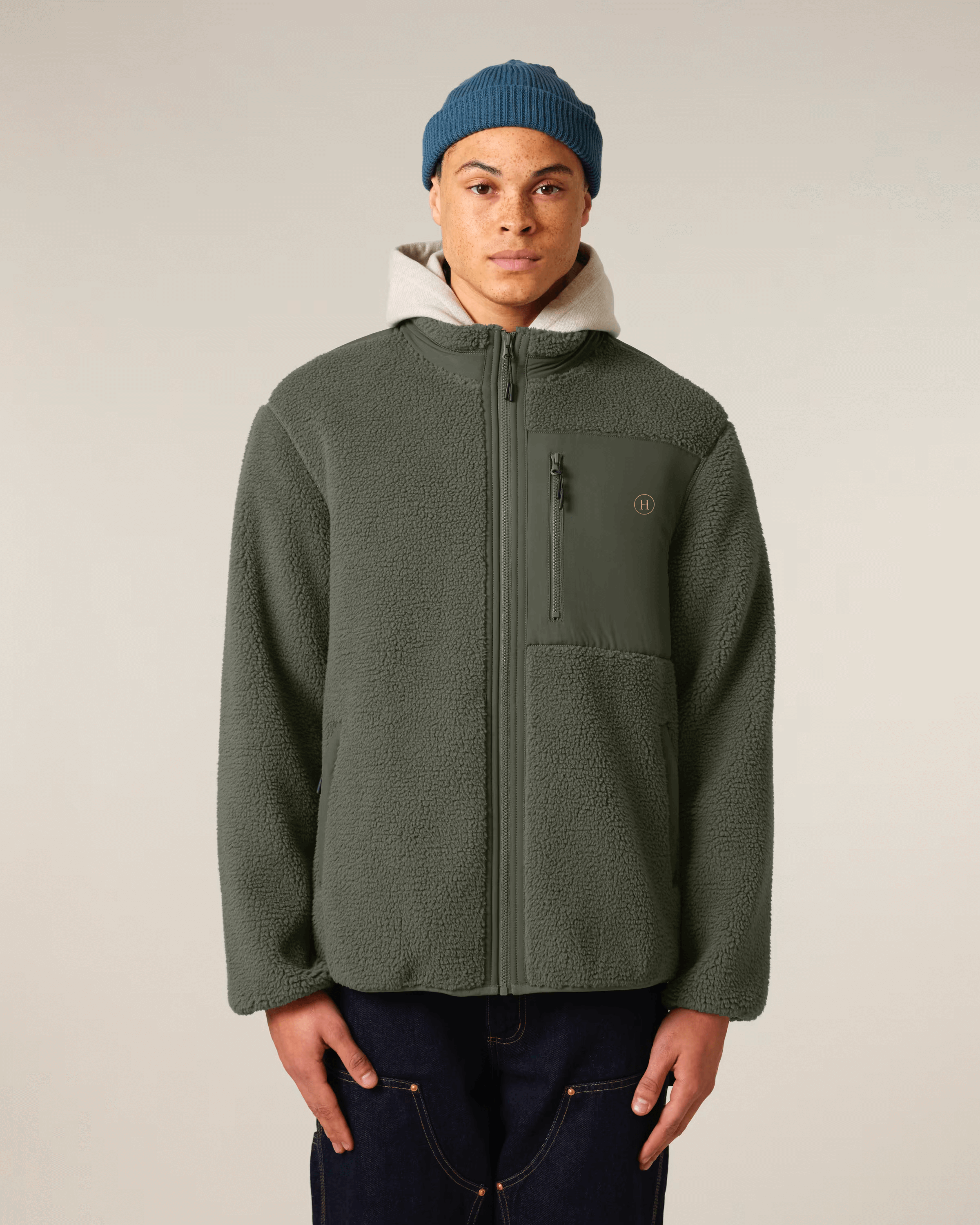 Person wearing a green jacket and blue beanie against a plain background