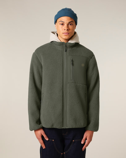 Person wearing a green jacket and blue beanie against a plain background