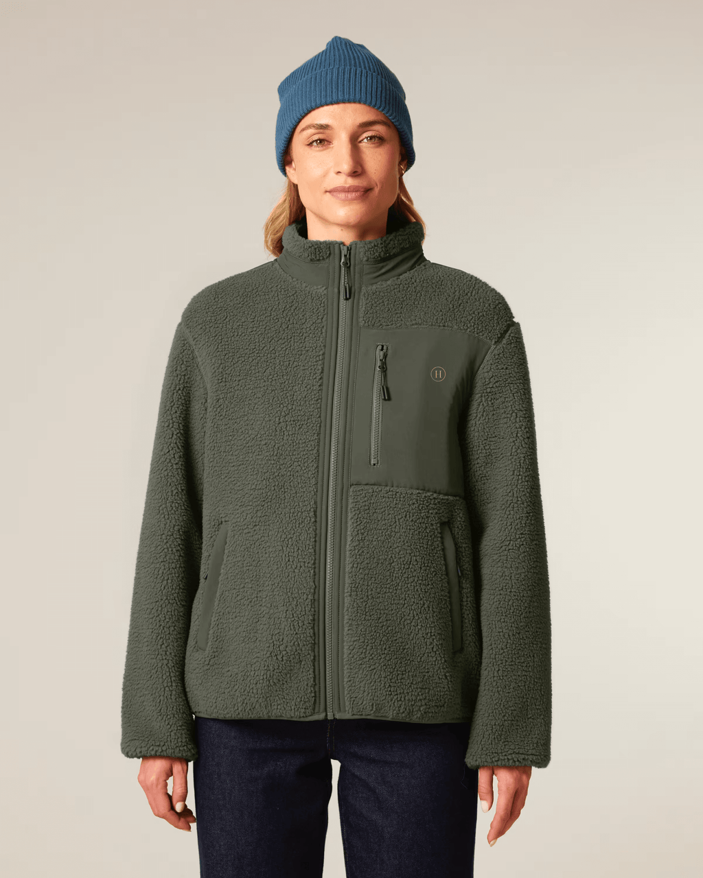 Person wearing a green jacket and blue beanie on a plain background