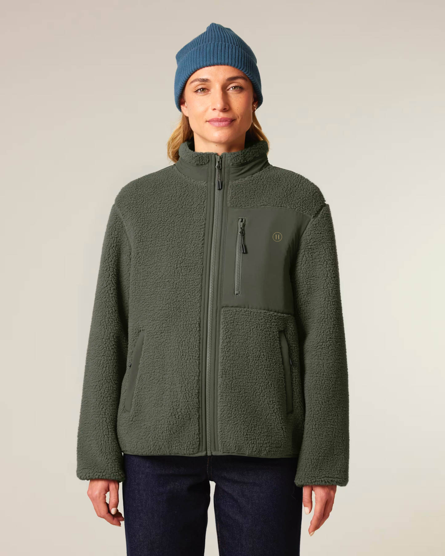 Person wearing a green jacket and blue beanie on a plain background