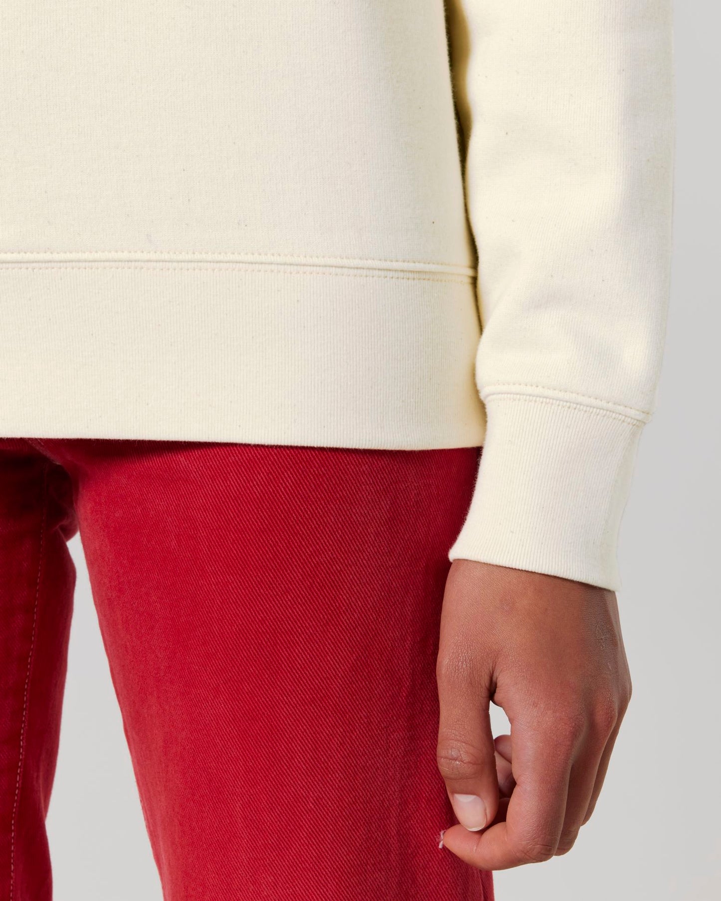 Person wearing a cream hoodie and red pants on a plain background