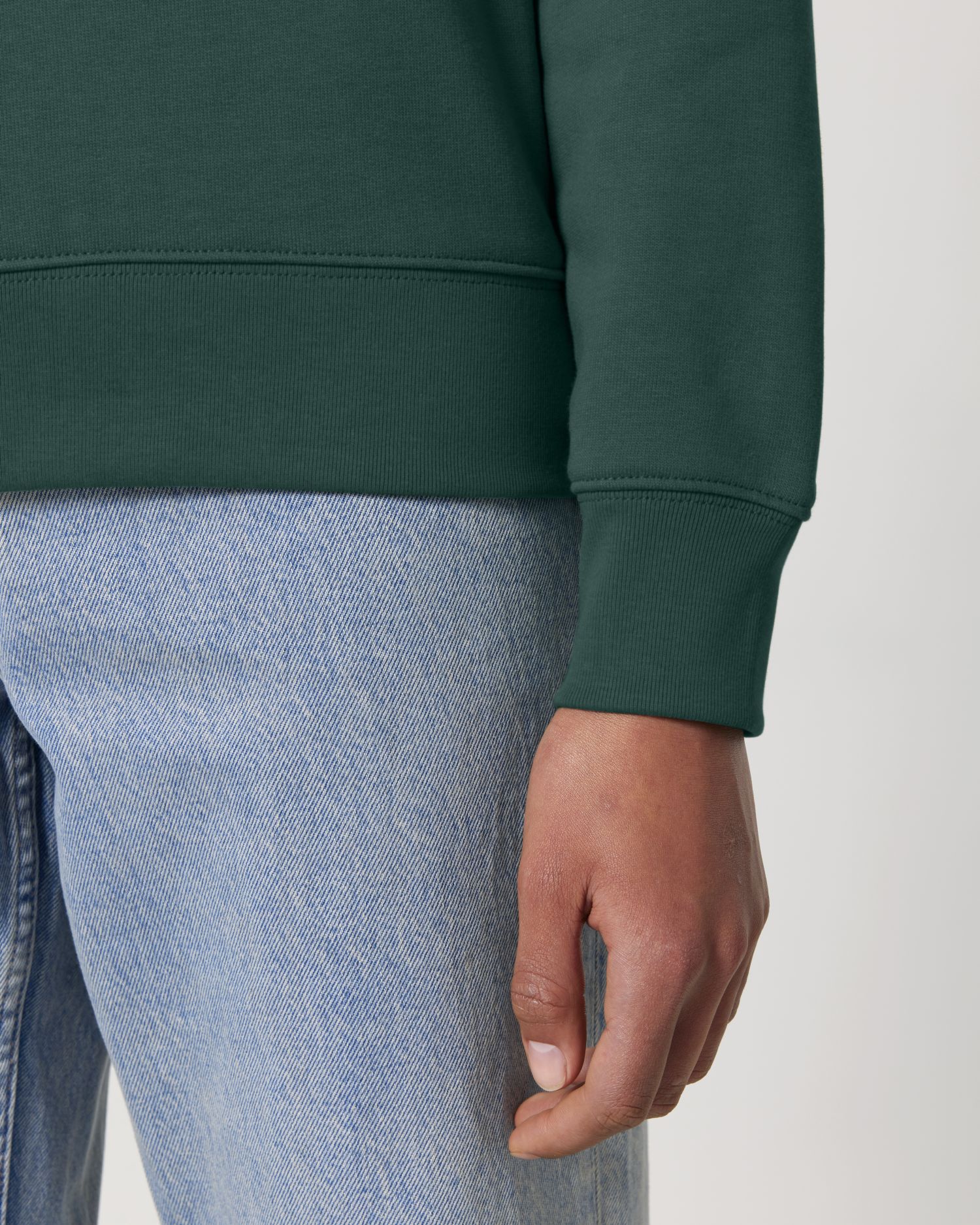 Person wearing a green sweatshirt and light blue jeans on a white background