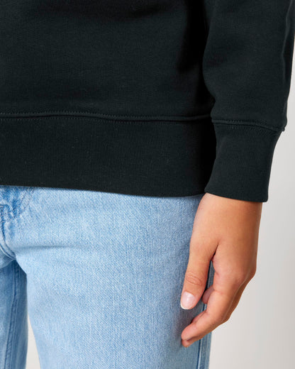 Person wearing a black sweatshirt and light blue jeans on a neutral background